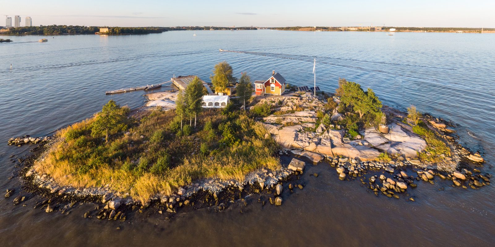 Katajanokanluoto 2 2021 08 30. Kuvaaja: Ilmakuva pienestä luodosta, jossa on muutamia puurakennuksia. Taustalla näkyy metsää ja rakennuksia. Vasemmassa reunassa kolme tornitaloa. Katajanokanluoto 2 2021 08 30. Kuvaaja: Ilmakuva pienestä luodosta, jossa on muutamia puurakennuksia. Taustalla näkyy metsää ja rakennuksia. Vasemmassa reunassa kolme tornitaloa.