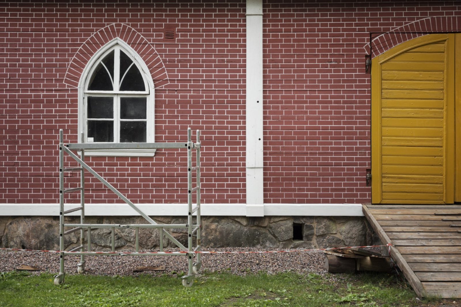 Punatiilen näköiseksi maalattua seinää, jossa ikkuna ja keltainen kaksoisovi. Ikkunan edustalla rakennusteline. Punatiilen näköiseksi maalattua seinää, jossa ikkuna ja keltainen kaksoisovi. Ikkunan edustalla rakennusteline.